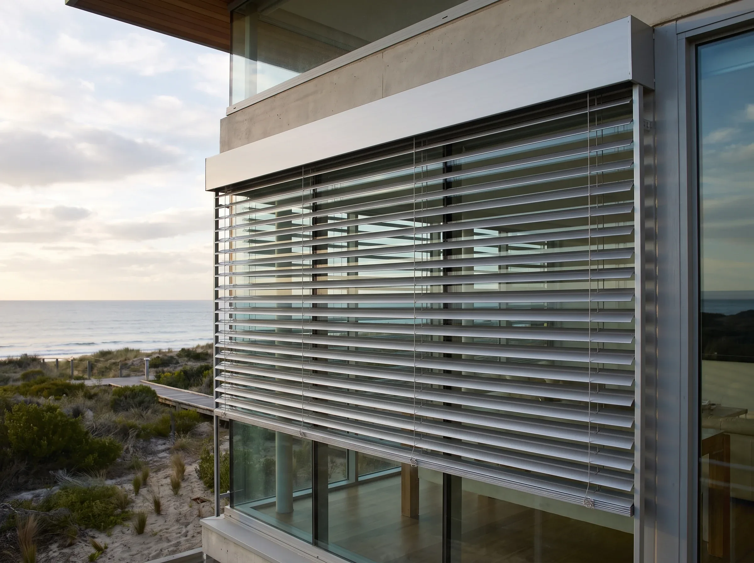 Aluminium external venetian blind slats with a motorised headbox mounted outside a Clifton glass wall